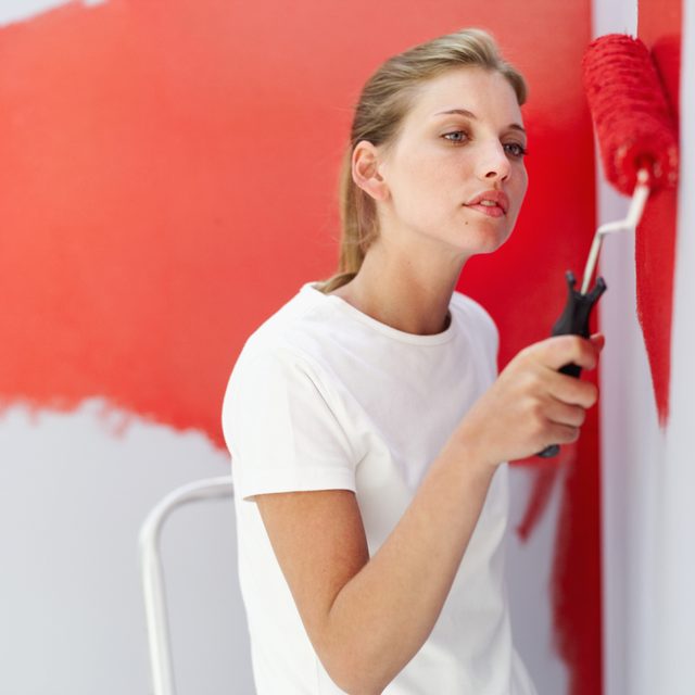 Close-up de la femme peignant un mur rouge.
