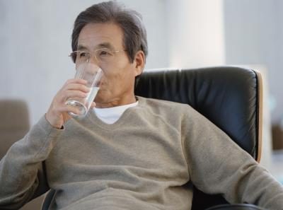 Un homme boit un verre d'eau dans un fauteuil.