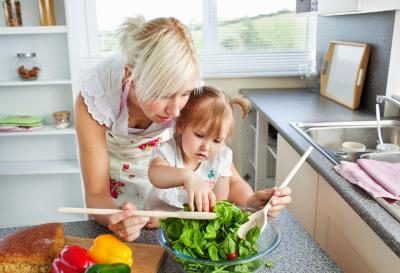 Une maman prépare une salade avec sa jeune fille.