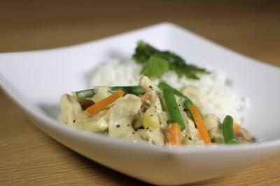 Une portion de curry vert de poulet avec du riz et des légumes sur une plaque.