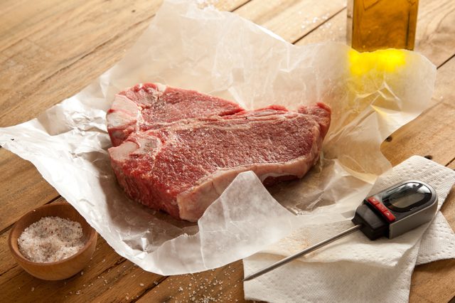 Steak cru sur du papier de boucherie à côté de thermomètre, l'huile d'olive et le sel.